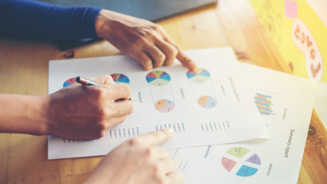 Cilvēki uz galda norāda uz lapām ar statistikas datiem