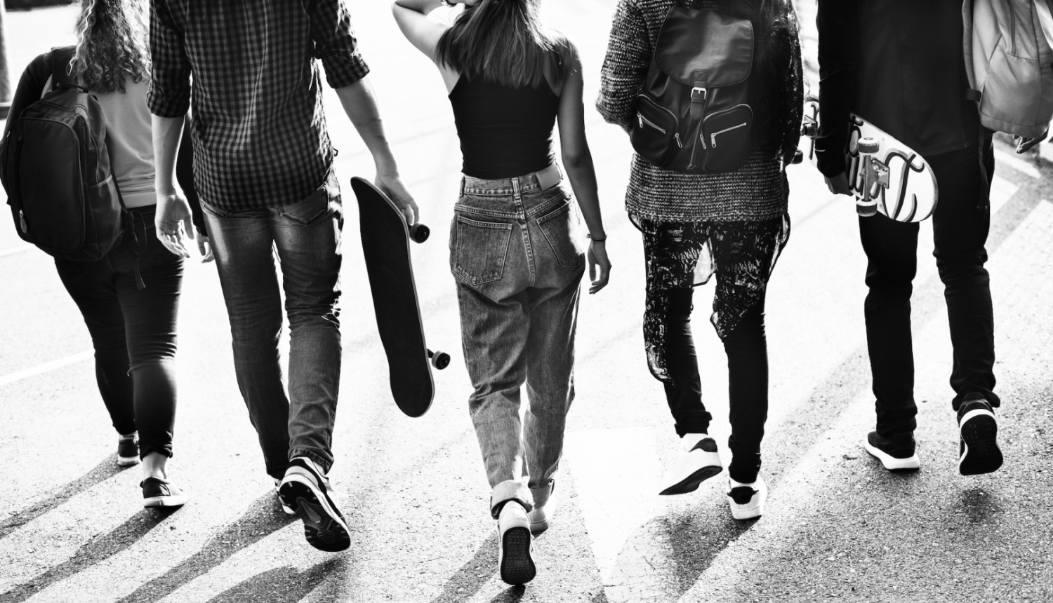 Jaunieši iet pa ielu, skats no muguras